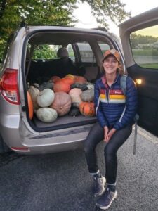 Libby sitting next to a van full of pumpkins and squash
